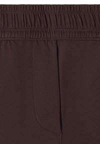 Gros plan de la ceinture élastique brun foncé et du détail du tissu du pantalon avec des coutures visibles et une couture avant.
