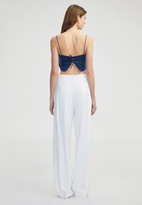 Námořnický sametový crop top s nastavitelným zavazováním na zádech, v kombinaci s bílými kalhotami s vysokým pasem a širokými nohavicemi, které mají zadní kapsy a hladkou texturu.