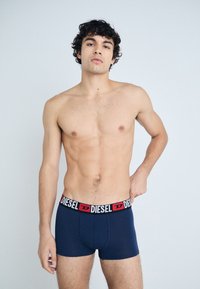 Boxers en bleu marine avec un élastique noir et rouge portant le logo "DIESEL". Texture lisse et coupe ajustée, design taillé.