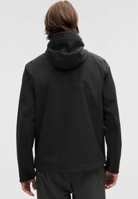 Svart, mjukt skaljacka med huva, med en stilren design och elastiska muddar. Slät textur, inga synliga mönster eller hårdvarudetaljer.
