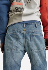 Ljusblå denimjeans har en traditionell femfickorsdesign, synlig sömnad och en märkesetikett på bakre midjebandet.