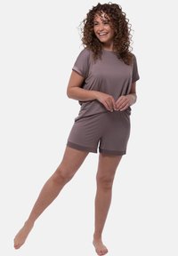 Completo in maglia marrone corto con un fit rilassato. La t-shirt ha le maniche arrotolate, e i pantaloni corti hanno i bordi a contrasto. Texture morbida con una leggera lucentezza.