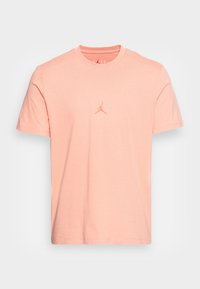 Camiseta de algodón de color rosa claro con cuello redondo, mangas cortas y un pequeño logo Jumpman en relieve en el pecho. Textura suave.