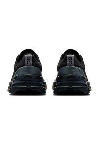 Chaussures de sport noires avec une tige en maille texturée, un talon rembourré et une semelle en caoutchouc mise en valeur. Présente une marque sur le talon et des nuances variées.