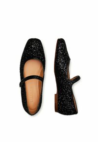 Zapatos Mary Jane negros con punta cuadrada, cubiertos de purpurina, con una correa en el empeine y una suela plana marrón. Forro interior suave.