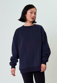 Felpa oversize blu navy con scollatura a girocollo, polsini e orlo a costine, con un logo goffrato discreto sul davanti.