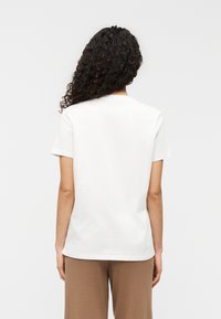 Άσπρο βαμβακερό T-shirt με κοντά μανίκια, στρογγυλή λαιμόκοψη και άνετη εφαρμογή. Ομαλή υφή, χωρίς ορατά σχέδια ή διακοσμήσεις.