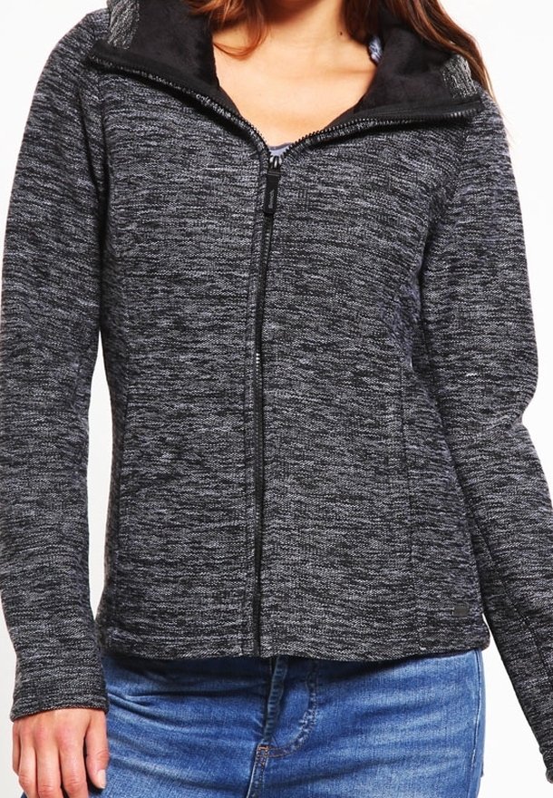 Femme portant une veste en maille gris foncé zippée à col montant et un jean bleu, montrée des épaules aux hanches.