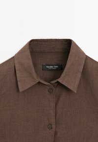 Brun linneskjorta med klassisk krage, knappstängning fram och en strukturerad tyg. Etiketten säger "Massimo Dutti."