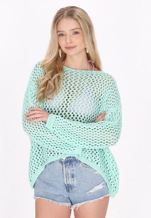 Maglione leggero, verde menta, a maglia aperta con maniche lunghe. Abbinato a pantaloni shorts in denim strappati a vita alta. Stile da spiaggia casual.