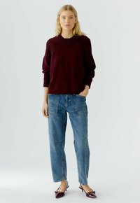 Burgundy knit sweater with ribbed neckline, paired with blue denim straight-leg jeans and maroon mules with bow accent.