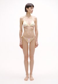 Bikiny sada so žltým trojuholníkovým vrchom zdobeným vírivým vzorom a zodpovedajúcim spodkom so zaväzovaním na bokoch a ružovým akcentom.