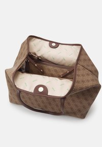 Brązowa torba typu tote z wzorem, o solidnej konstrukcji, z kremowym wnętrzem i zielonymi logo "GUESS", srebrnymi elementami metalowymi oraz zatrzaskiem.