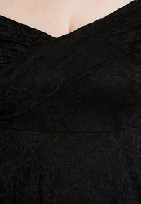 Svart spetsklänning med en korsad bystdesign, som har detaljerade blommönster och texturerat tyg, som betonar en figurnära silhuett.