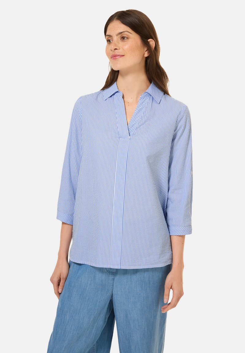 Camicia a maniche lunghe a righe blu e bianche, con colletto e scollatura a V. Tessuto morbido con una vestibilità rilassata, abbinata a pantaloni larghi azzurri.