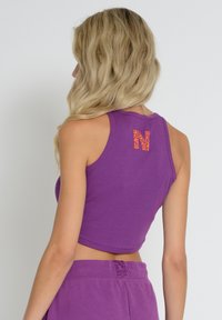 Purple ribbed crop top with a round neckline and a patterned "N" logo in orange on the back. The fabric has a soft texture.