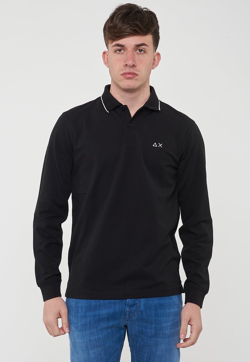 Polo a maniche lunghe nera con colletto bianco ricamato e un piccolo logo sul lato sinistro del petto. Abbinato a jeans blu.