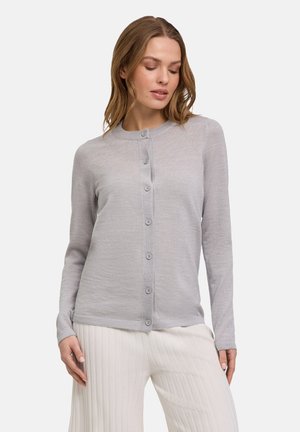 Hellgraue, langärmlige Strickjacke mit Rundhalsausschnitt, Knopfverschluss und glatter Textur. Über plissierten weißen Hosen getragen.
