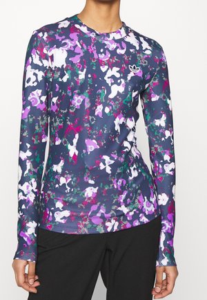 Chemise à manches longues avec motif floral abstrait bleu, violet, blanc et vert et petit logo trèfle blanc sur la poitrine.