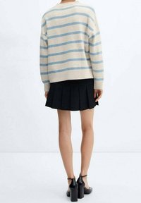 Maglione crema con righe blu, vestibilità morbida e orlo a costine, abbinato a una gonna a pieghe nera e scarpe con tacco nere.