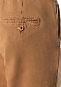 Des pantalons en coton marron présentent une poche diagonale avec une fermeture à bouton. Le tissu a une texture lisse et un éclat subtil.