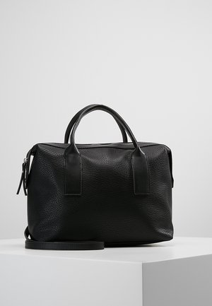 Czarna torebka ze strukturalnej skóry z podwójnymi uchwytami i paskiem na ramię, wyeksponowana na białym cokole na jednolitym jasnoszarym tle.