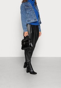 Veste en jean sur un col roulé bleu, pantalon en simili cuir noir, bottes à talons noires et un sac à main noir brillant avec une texture crocodile.