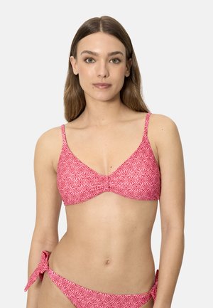 Mujer con cabello liso y castaño, vestida con un top de bikini rosa con estampado y bragas de bikini a juego con lazos laterales, posando contra un fondo liso.