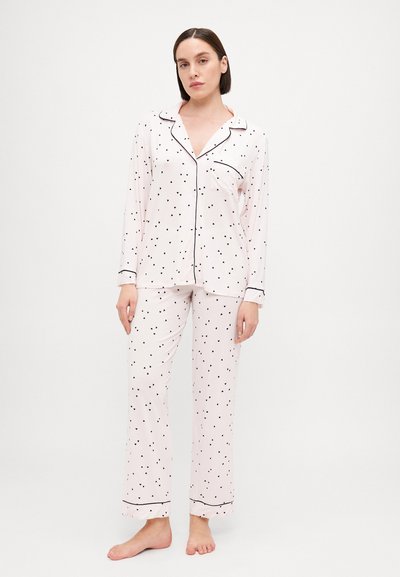 Light pink pajama set with black heart prints, long sleeves, and black piping details. The top features a pocket; pants are loose-fitting.