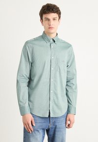 Lysegrønn skjorte med knapper laget av vevd stoff, med en liten lomme og krage, sammen med blå jeans.