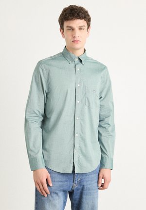 Camicia button-up verde chiaro in tessuto intrecciato, con una piccola tasca e colletto, abbinata a jeans blu.
