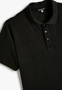 Svart polo nacktröja i strukturerad väv, med en vikbar krage, treknappslå och korta ärmar.