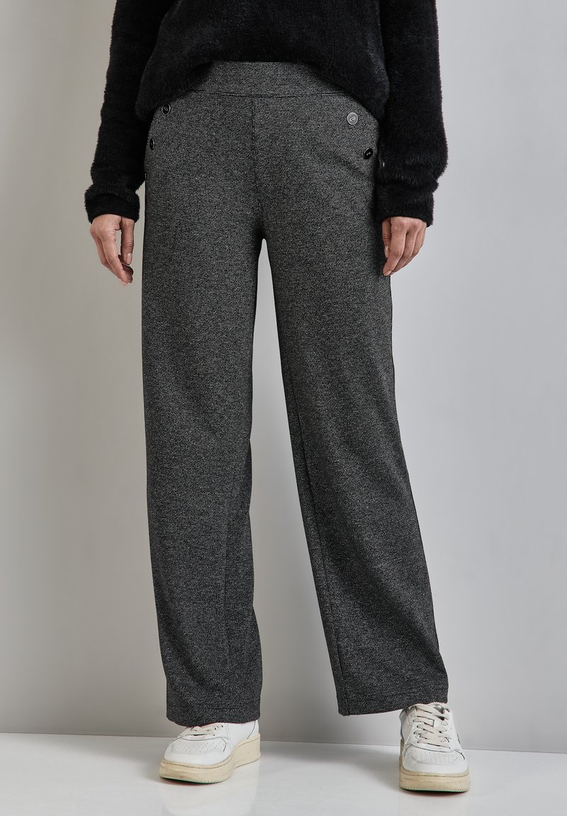 Pantaloni grigi a gamba larga realizzati in tessuto texturizzato, con tasche anteriori con chiusura a bottone e una vita liscia. Abbinati a sneaker bianche.