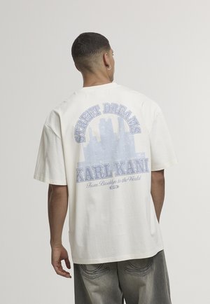 Baltas medvilninis marškinėlis su grafiniu dizainu, mėlynu tekstu ir miesto siluetu ant nugaros. Trumpomis rankovėmis ir laisvo kirpimo.