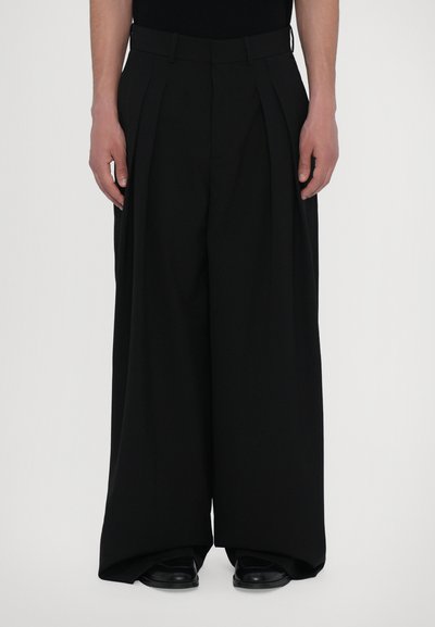 Zwarte geplooide broek met een wijde pijpdesign, gemaakt van een gladde stof. Heeft een aansluitende taille en is gestyled met zwarte schoenen.