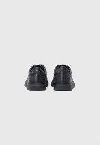 Schwarze Sneakers mit einem Obermaterial aus strukturiertem Leder, flacher Gummisohle und minimalen Branding-Akzenten. Rundes Zehendesign mit gepolstertem Fersenbereich.