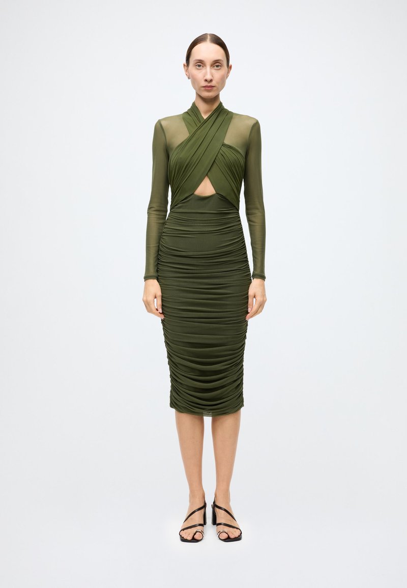 Robe vert olive avec manches longues en tissu transparent, texture froncée, corsage croisé et détail découpé. Finition avec une jupe ajustée à longueur genou.