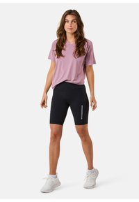 Lys lilla kortærmet v-hals top parret med tætsiddende sorte shorts med en reflekterende stribe. Modellen har hvide træningssko på.