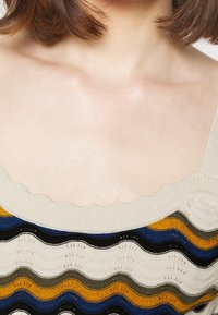 Pletený top v krémové barvě, s vlnitými pruhy v modré, zelené, černé a zlaté. Výstřih s obloukovými okraji a texturovaná látka s detaily otevřeného stehu.