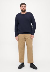 Námořnický textured svetr s kulatým výstřihem, v kombinaci s béžovými rovnými chinos kalhotami a černými šněrovacími botami. Čistý, minimalistický vzhled.