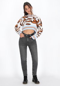 Trui met een cropped ontwerp, voorzien van een luipaardprint in oranje en bruin op een witte basis, gecombineerd met hoge zwarte jeans en zwarte laarzen.