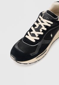 Fekete és szürke Polo sneaker fehér fűzőkkel, hálós és velúrbőr felsőrésszel, látható talp légpárnával, valamint Polo logóval az oldalon és az orrán.