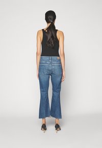 Jeans de mezclilla oscuros y acampanados con un dobladillo deshilachado, que cuentan con una cintura de altura media, bolsillos traseros y detalles de costura visibles. Combinados con una camiseta sin mangas negra.