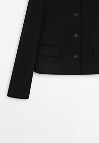 Veste noire en laine sur mesure avec manches longues, poches avant à rabat et trois boutons noirs au centre.