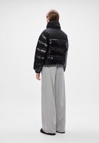 Melnā pūkainā jaka ar spīdīgu apdari, kurai ir pārspīlēta šuvēšana un augsts apkakle, apvienota ar vaļīgām pelēkām sporta biksēm un melniem apaviem.