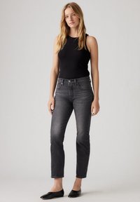 Top in tessuto a coste nero abbinato a jeans in denim grigio, con un design aderente, stile a cinque tasche e gamba leggermente affusolata. Ballerine nere.