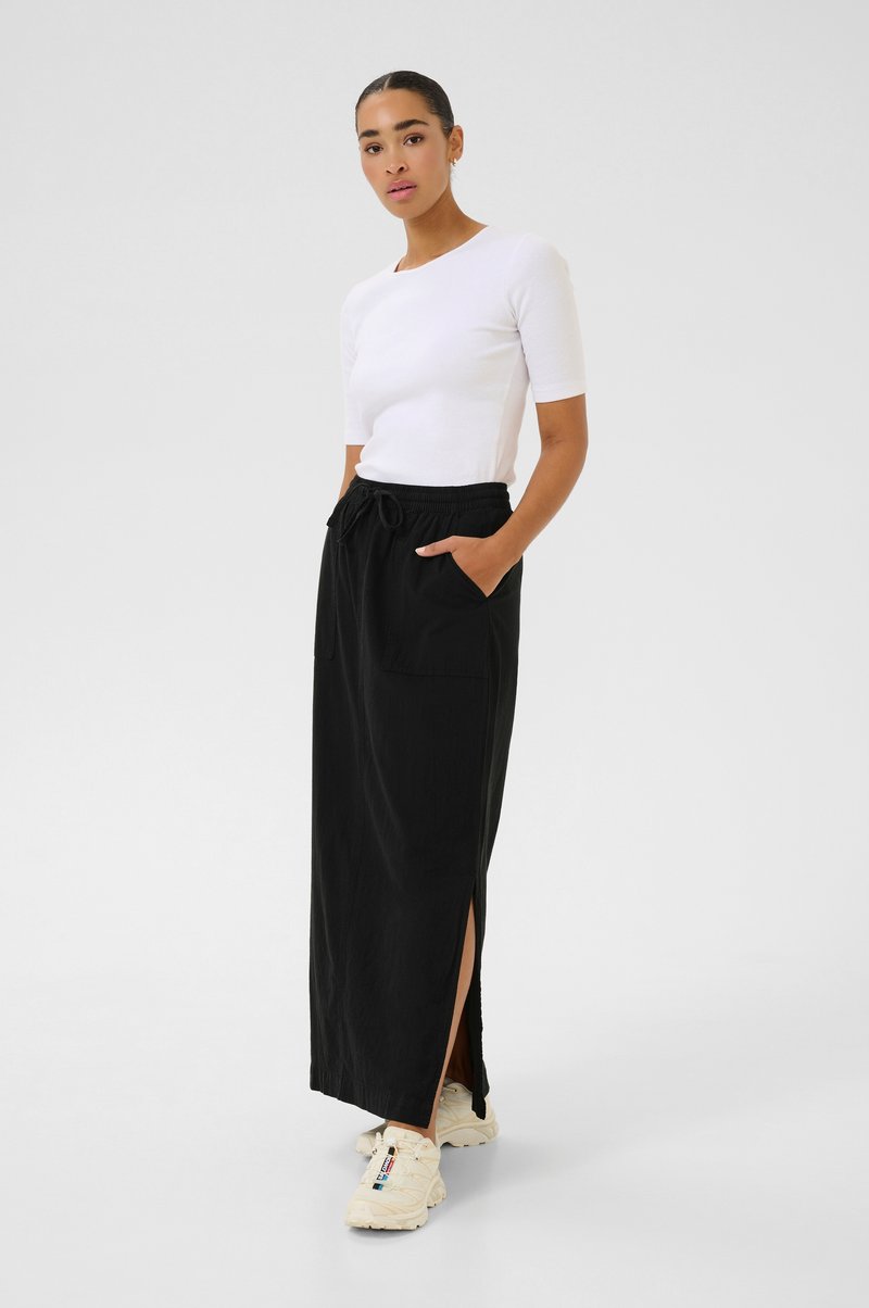 Jupe maxi noire avec fentes latérales, dotée de deux poches avant et d'une taille élastique. Associée à un haut blanc ajusté à manches courtes.