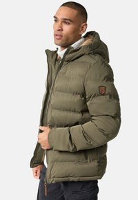 Olivengrønt puffer-jacke med hætte, med et stikmønster, lynlåslukning og et brændmærket læderlap på ærmet.