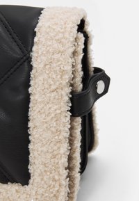 Svart läderväska med en plysch, beige krullig inredning. Har silverdetaljer och ett lock med tryckknappsstängning.