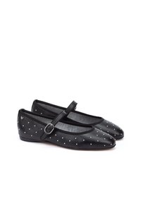 Bailarinas negras con punta afilada, que cuentan con una correa con hebilla, decoradas con tachuelas plateadas a lo largo de la superficie superior. Textura suave.